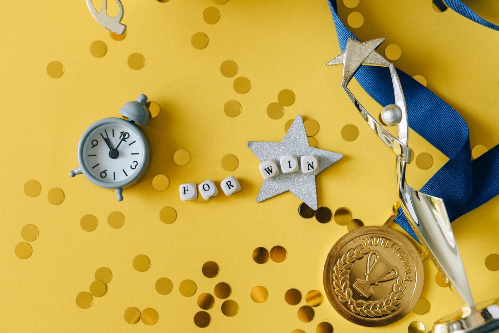 Photo by Nataliya Vaitkevich Conceptual flat lay of a trophy, medal, and clock with 'FOR WIN' letters, symbolizing victory and achievement.